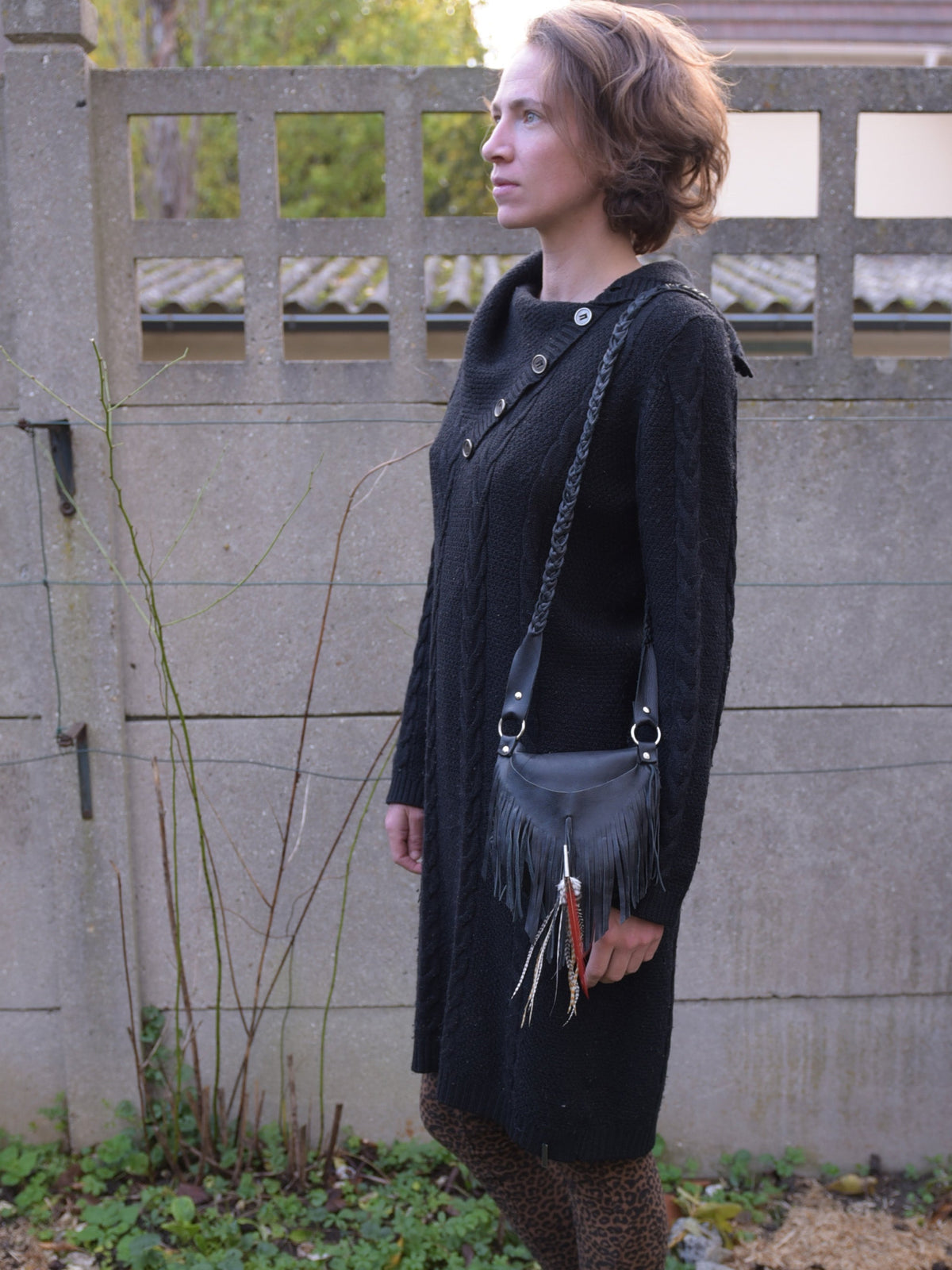 Ruby Feathers Achack black leather fringe bag with metallic accents worn by a woman in a black sweater dress