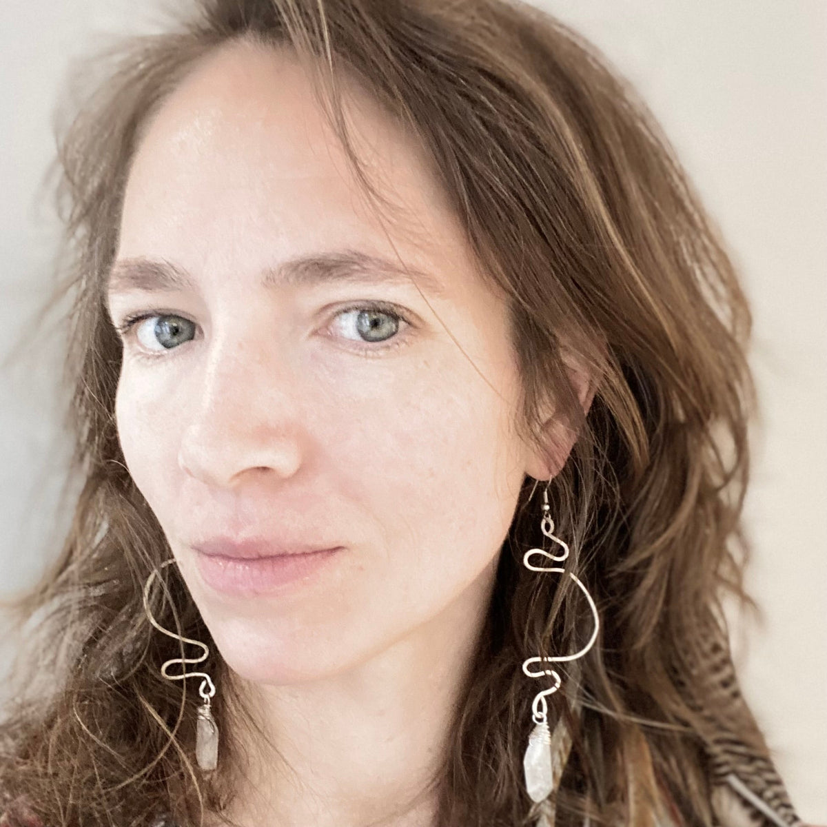 Ruby Feathers Waveform Whispers earrings featuring handpounded silver-covered copper wire and crystals on a woman.