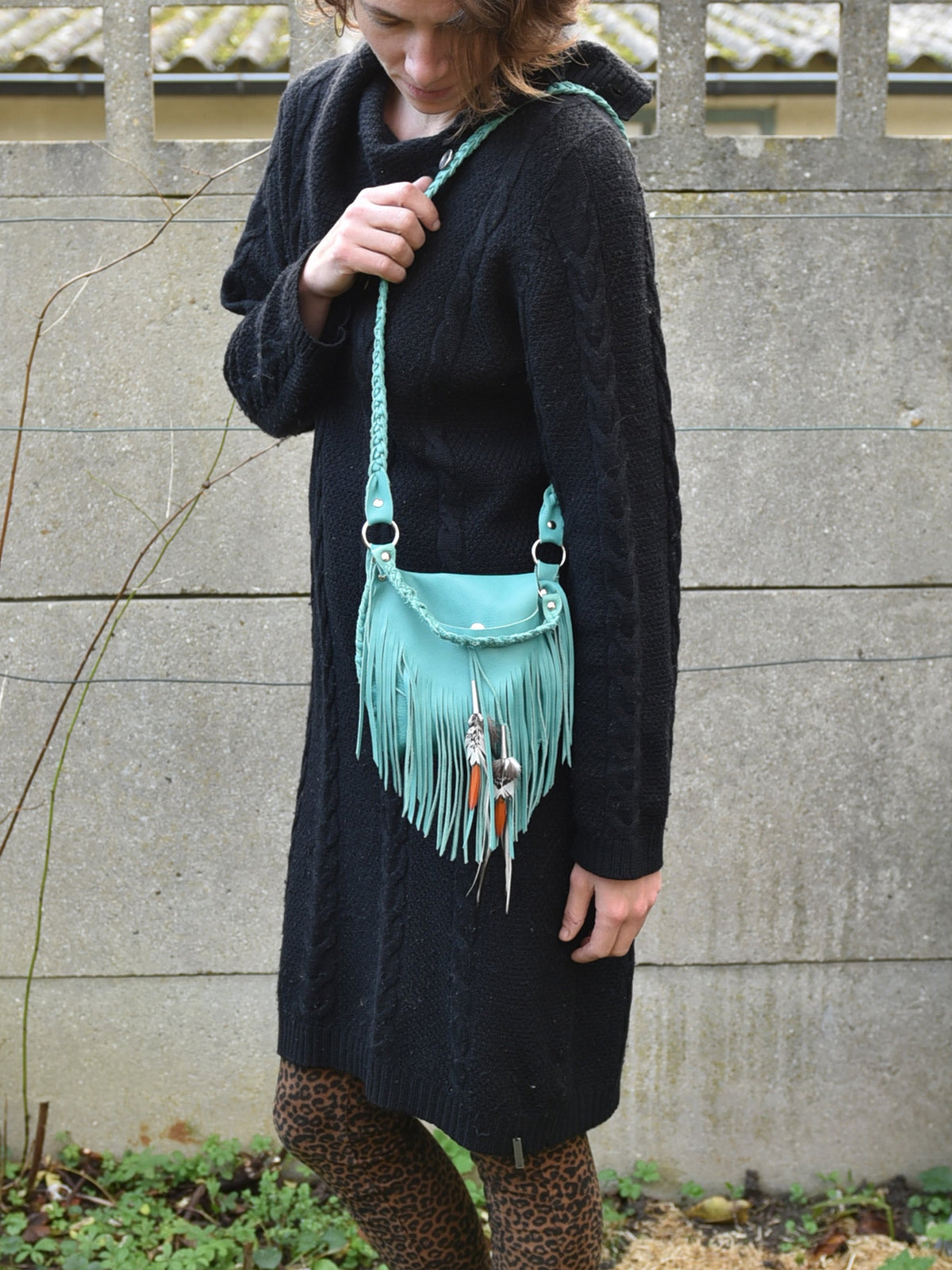 Ruby Feathers Achack turquoise leather fringe bag with metallic charms worn by a woman in a black sweater