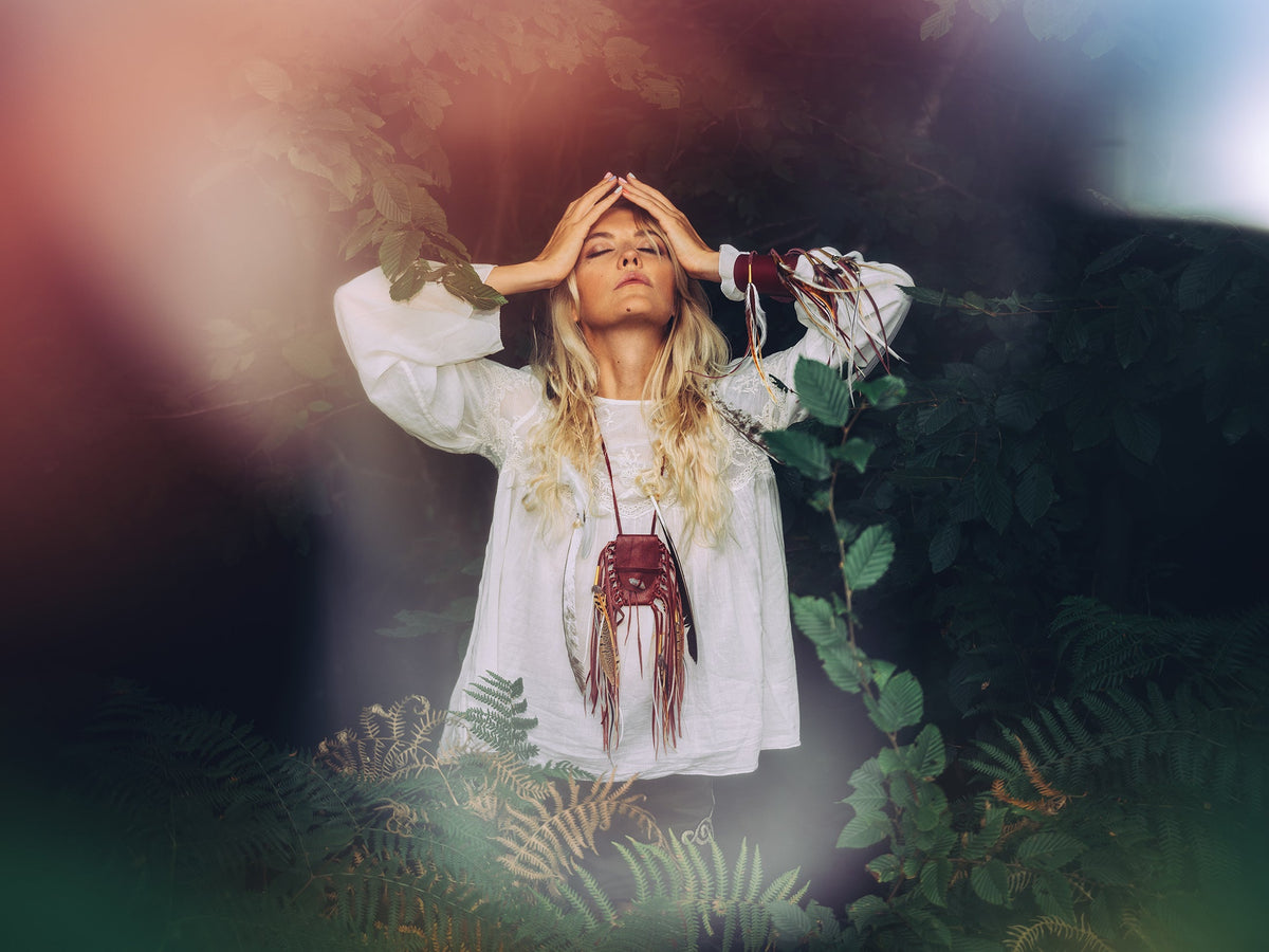 Ruby Feathers bohemian cuff worn by a woman in a white blouse, featuring hand-cut calfskin leather and flowing plumes.