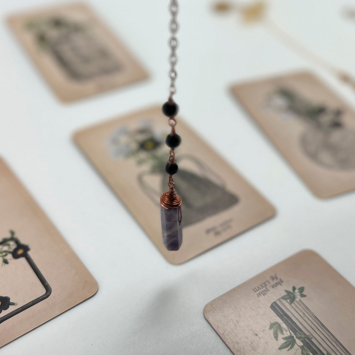 Ruby Feathers Celestial Calm pendulum with cloud agate point, amazonite beads, and silver spiral over tarot cards.