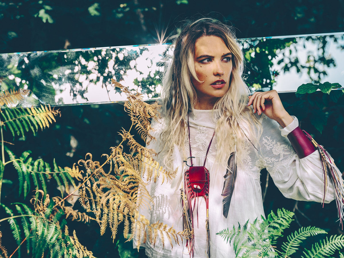 Ruby Feathers bohemian cuff made of supple calfskin leather and flowing feathers worn by a woman in a forest setting
